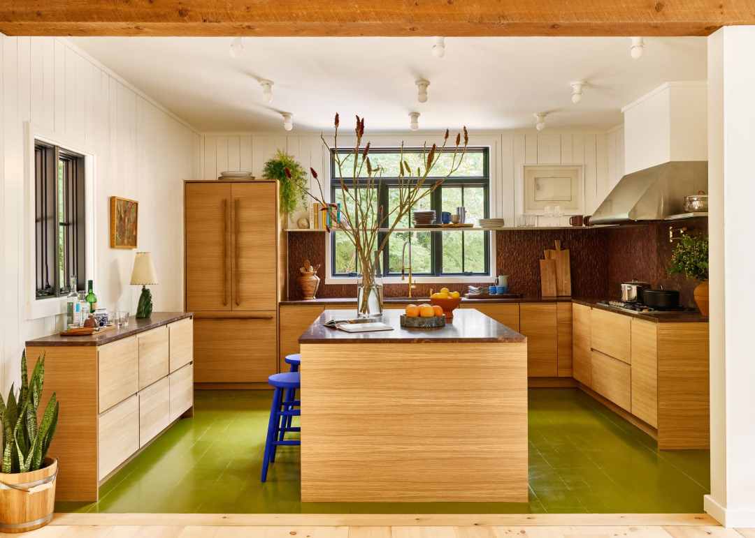 A warm oak modern kitchen with green floor and textured deep terracotta tiled backsplash. The cabinet doors are ReformCPH.