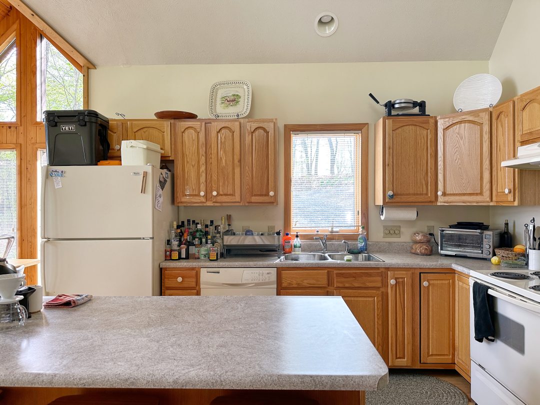 Dated honey oak cabinets and formica countertops with white appliances in an early 2000s kitchen.