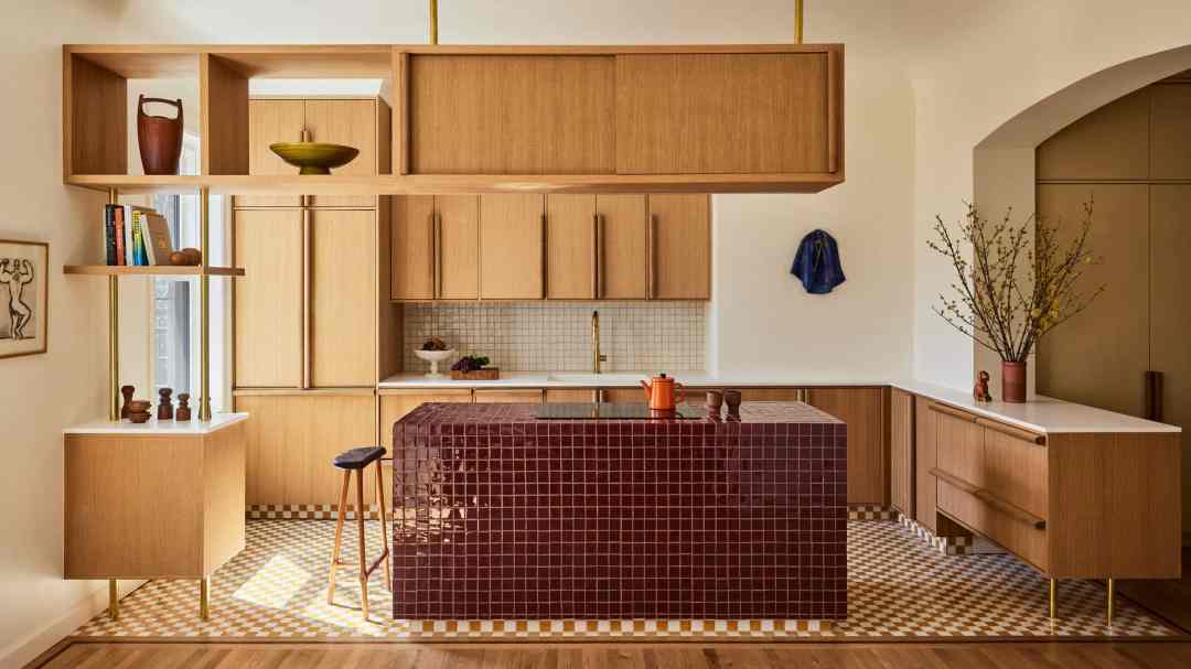 A modern kitchen with warm oak cabinets with chunky wood handles, and a brick red tiled island.